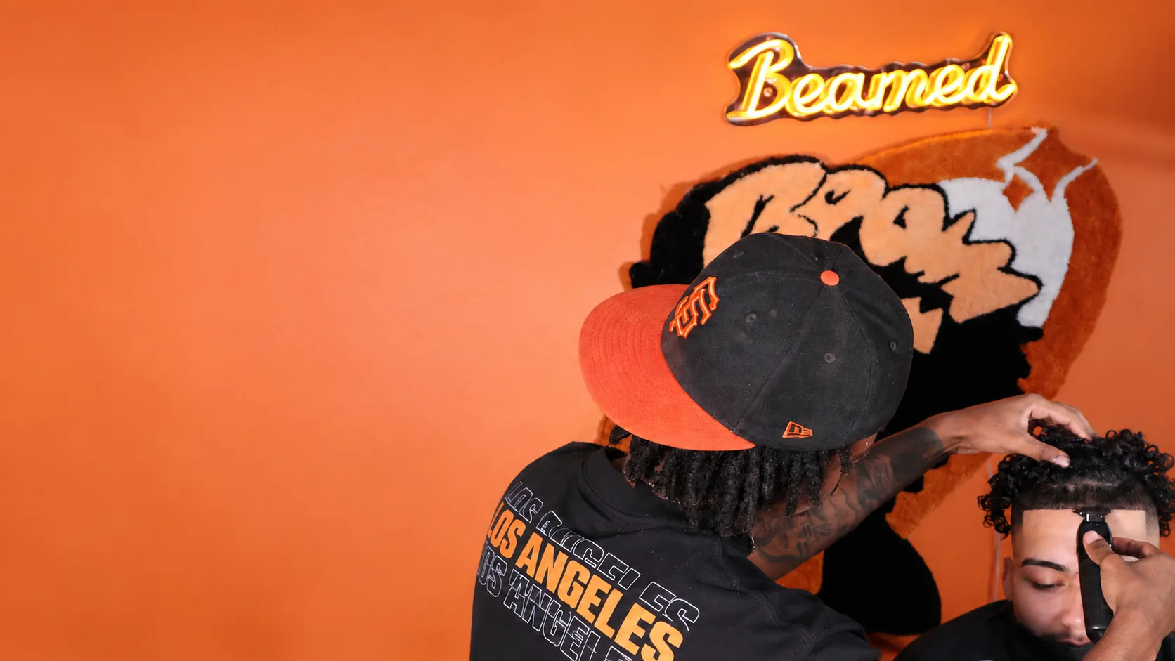 A Beam0 barber lining up a client in front of an orange wall with a neon Beamed sign